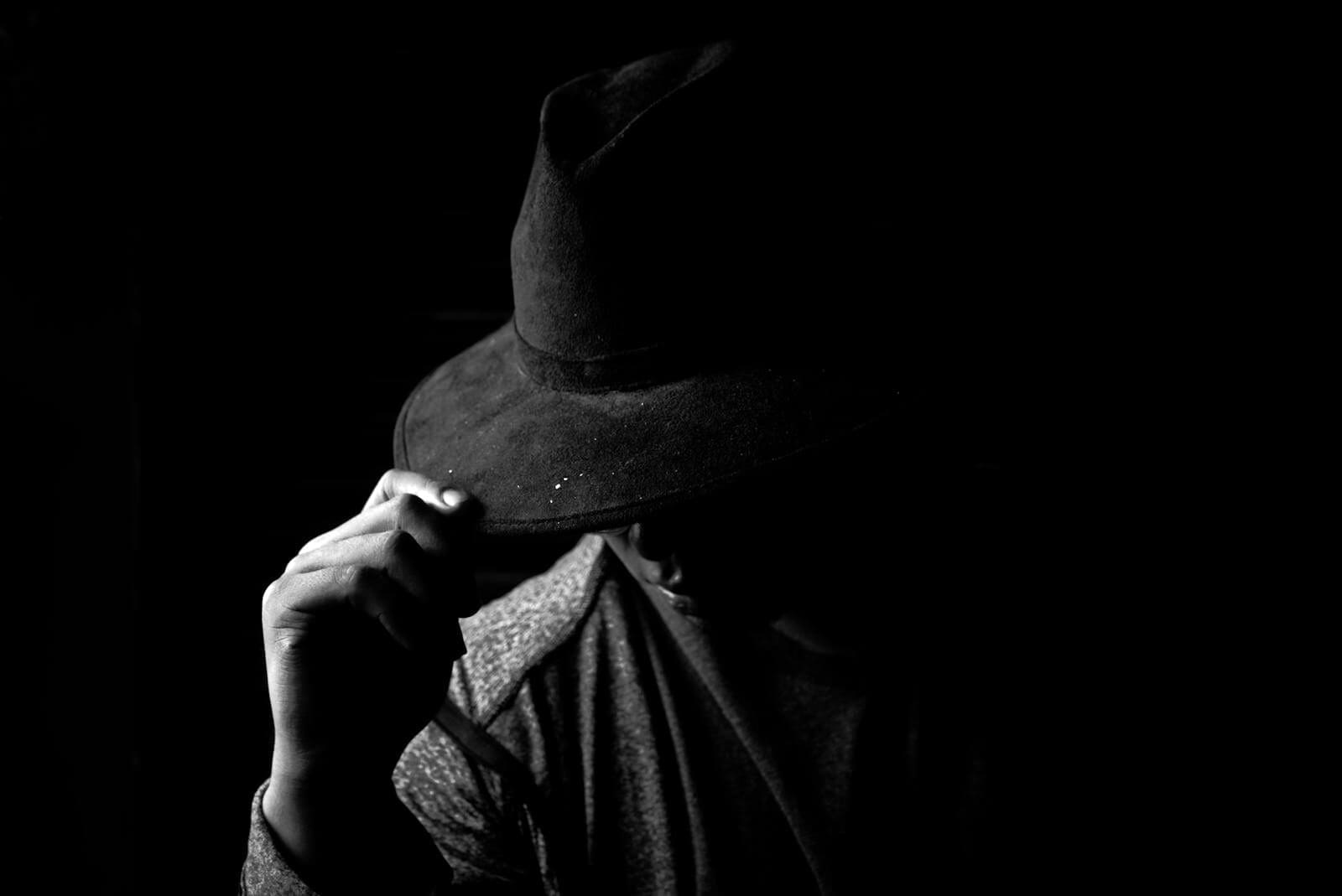 A dramatic black and white portrait of a person wearing a hat, creating a mysterious mood.