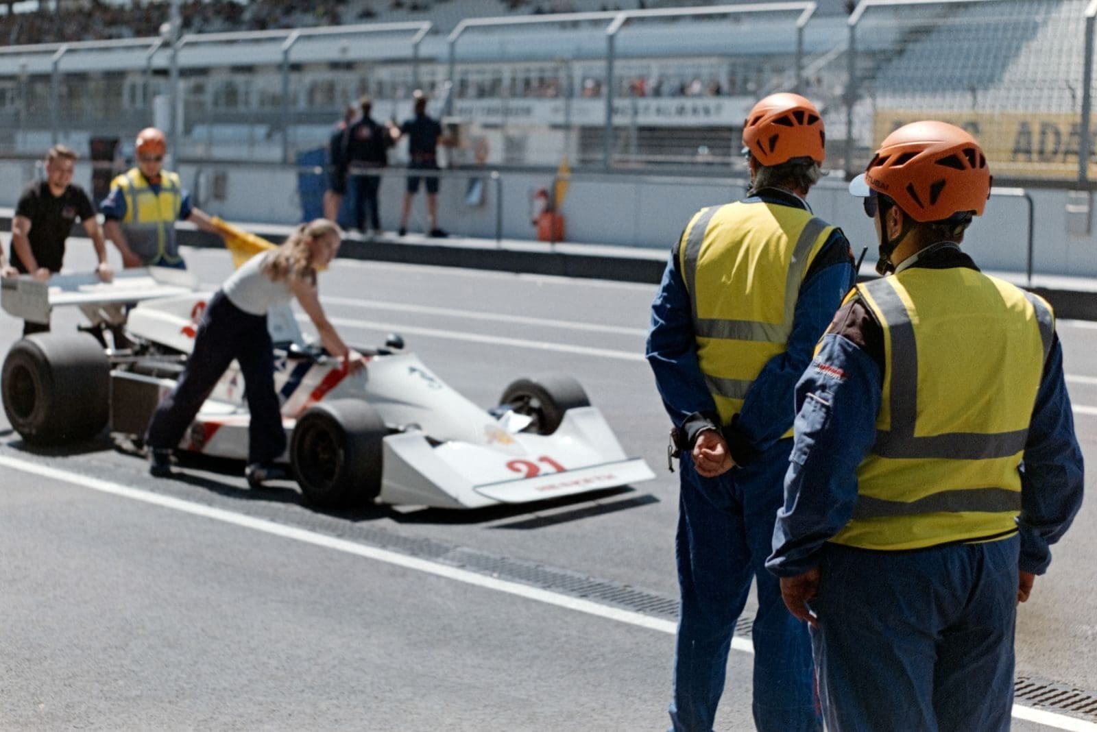 Race car being wheeled to pit stop with crew in helmets and safety vests.